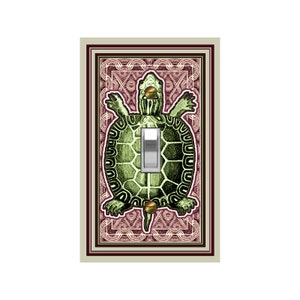 May include: A light switch cover featuring a green turtle with a brown shell and a gold accent. The turtle is surrounded by a pink and white patterned border.