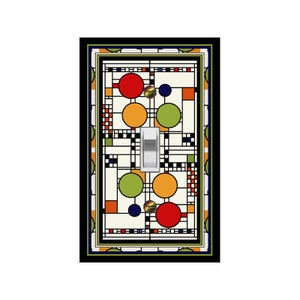 May include: A light switch cover with a geometric design featuring circles in red, orange, green, and blue on a white background. The design is framed with a black border.