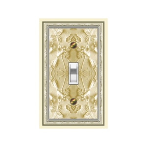 May include: A decorative light switch cover with a floral embossed design in shades of gold and cream. The switch plate has a rectangular shape with a silver toggle switch in the center. The design includes a cream-colored border.
