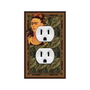 May include: White electrical outlet cover featuring a portrait of a woman with a monkey, set against a backdrop of green leaves. The artwork is framed in a brown border.