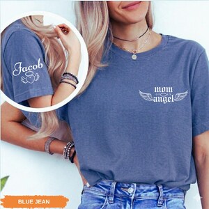 A woman wearing a blue t-shirt with the text "Mom of an Angel" printed on it, along with a necklace and bracelets.