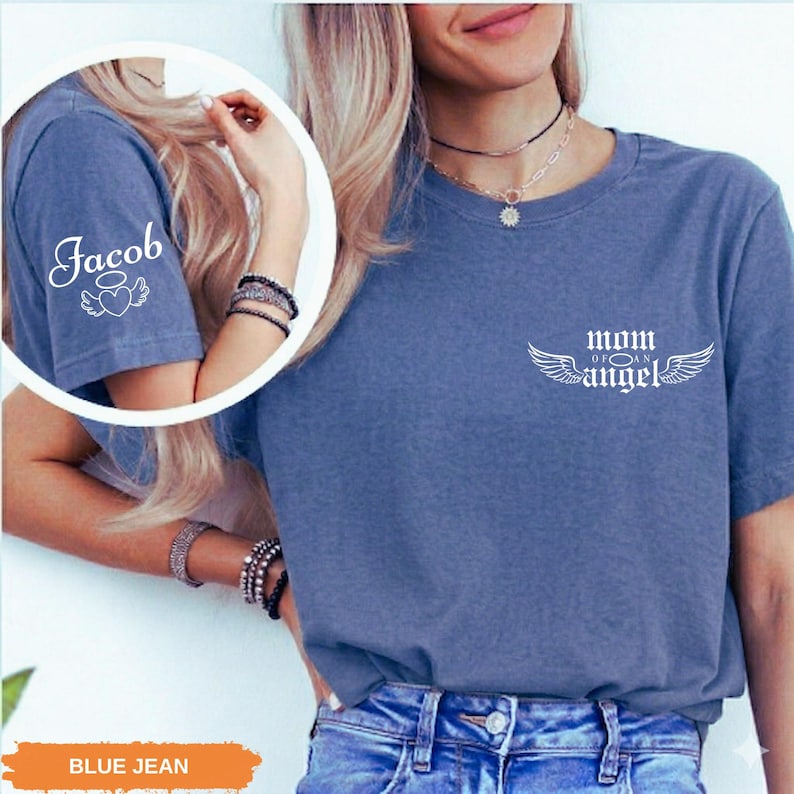 A woman wearing a blue t-shirt with the text "Mom of an Angel" printed on it, along with a necklace and bracelets.