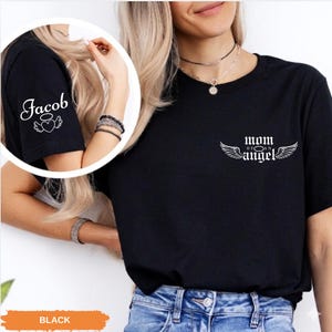 A woman wearing a black t-shirt with the text "Mom Angel" printed on it, along with a necklace.