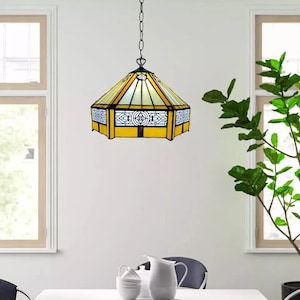 Puede incluir: Una lámpara colgante de vidrio Tiffany con un diseño geométrico amarillo y blanco. La luz cuelga de una cadena y está suspendida del techo.