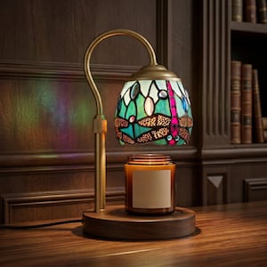 Peut inclure: Une lampe chauffe-bougie avec un bras métallique courbé couleur laiton et une base circulaire en bois. La lampe présente un abat-jour en vitrail orné d'un motif de libellule dans des tons turquoise, vert et magenta, placé au-dessus d'une bougie.