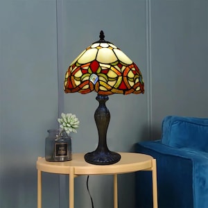 Peut inclure: Une lampe de table en verre Tiffany avec une base en métal noir. L'abat-jour présente un motif géométrique dans des tons de rouge, jaune, vert et bleu.