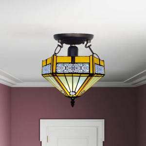 May include: A yellow and white stained glass ceiling light fixture with a geometric design. The fixture has a black metal frame and hangs from the ceiling.