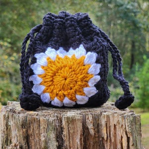 May include: A black crocheted drawstring bag with a white and yellow flower design.