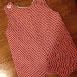 May include: A red and white gingham overall romper with white buttons.