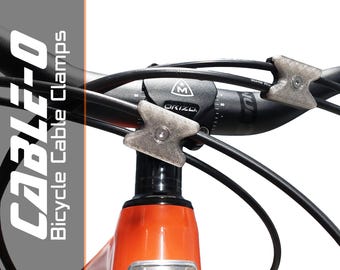 May include: A bicycle handlebar with black cables held in place by grey cable clamps. The clamps have an arrow-like design. The bike frame is orange. The text "CABLEO Bicycle Cable Clamps" is visible.