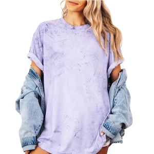 Puede incluir: Una camiseta de color lavanda con estampado tie-dye, de corte holgado y mangas cortas. La camiseta está hecha de una tela suave y cómoda y tiene un estilo casual y sin esfuerzo.