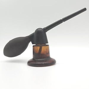 May include: A brown glass atomizer with a black plastic bulb and a long black plastic nozzle. The atomizer is filled with a brown liquid.