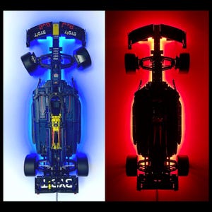 May include: A detailed model of a Formula 1 race car, illuminated with blue and red LED lights. The car features sponsor logos and intricate detailing, showcasing its aerodynamic design. The image is split, with one side lit in blue and the other in red.