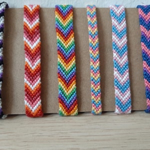 Pode incluir: Seis pulseiras de amizade coloridas com padrões de chevron. As pulseiras são feitas com fio de bordar e são de cor preta, branca, vermelha, laranja, amarela, verde, azul e roxa.