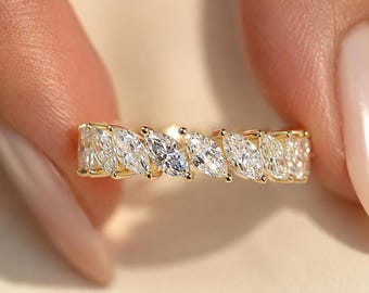 May include: A gold band ring featuring a continuous row of marquise-cut clear stones set in a shared prong setting. The stones are arranged horizontally, creating a repeating leaf-like pattern across the entire circumference of the metal band.