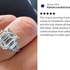 May include: A silver ring with a large, rectangular, emerald-cut center stone and smaller side stones. The ring is on a finger, showcasing its sparkle and design. The ring is made of 925 silver.