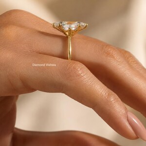 May include: A gold ring with a large, flower-shaped gemstone setting. The ring is on a person's hand, with the focus on the ring's intricate design and the sparkle of the gemstones. The ring is a piece of jewelry.