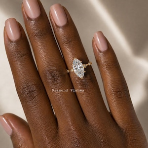 May include: A gold ring with a large, marquise-cut diamond as the centerpiece. The ring has smaller diamonds on the band and is set against a dark skin tone. The text "Diamond Vishwa" is visible.
