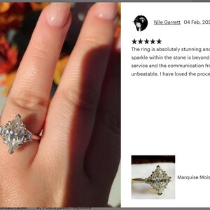 May include: A marquise moissanite engagement ring with a silver band. The ring features a large, sparkling, marquise-cut center stone and smaller side stones. The ring is shown on a person's finger.