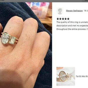 May include: A gold ring with an oval-cut diamond and an emerald-cut diamond. The ring is on a person's finger. The ring is a Toi Et Moi style. The ring is set with diamonds. The ring is a piece of jewelry.