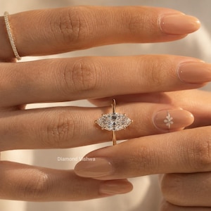 May include: A close-up of a hand wearing a gold ring with a large, oval-shaped diamond center stone and two smaller side stones. A smaller gold band with small diamonds is on the adjacent finger. The ring is set against a background of a person's skin.