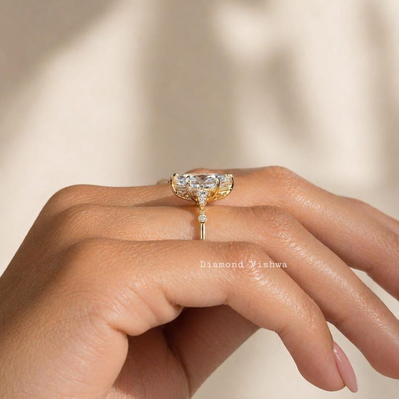 May include: A gold ring with a large, clear, rectangular-cut center stone and smaller accent stones. The ring has a detailed setting and a delicate band. The text "Diamond Vishwa" is visible.