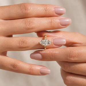 May include: A gold ring with a marquise-cut diamond center stone and smaller accent diamonds. The ring is held between two hands. The text "Diamond Vishwa" is visible on the ring.
