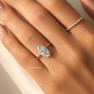 May include: A gold ring with a marquise-cut diamond is displayed on a hand. The diamond is the focal point, reflecting light. A second, smaller ring with small diamonds is also visible. The text "Diamond Vishwa" is at the bottom.