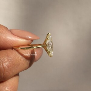May include: A gold ring featuring a large, marquise-cut diamond. The ring has an ornate, filigree design around the diamond and along the band. The ring is held up, showcasing the intricate details and sparkle of the gemstone.