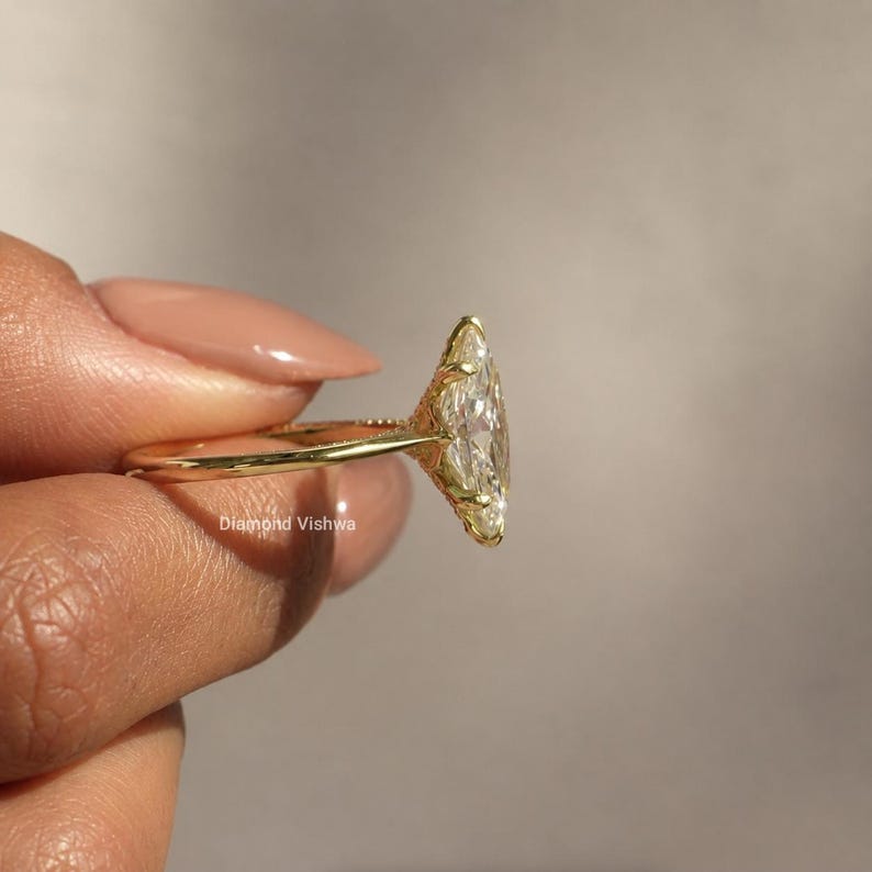 May include: A gold ring featuring a large, marquise-cut diamond. The ring has an ornate, filigree design around the diamond and along the band. The ring is held up, showcasing the intricate details and sparkle of the gemstone.