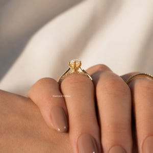 May include: A gold engagement ring with a large, round diamond center stone. The band is also adorned with smaller diamonds. The ring is on a person's finger. The text "Diamond Vishwa" is visible.