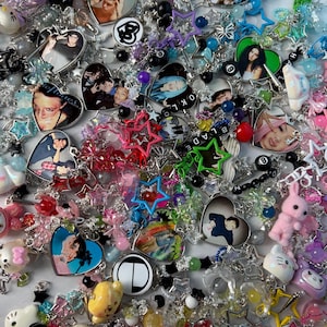 May include: A collection of colorful beaded jewelry, including necklaces and bracelets. The pieces feature heart-shaped pendants with images, star-shaped charms, and various other decorative elements. The color palette includes pink, blue, green, and clear beads.