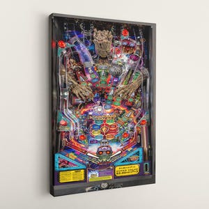 Może przedstawiać: Oprawiony wydruk artystyczny automatu do gry w pinball Strażników Galaktyki. Grafika przedstawia kolorowy wzór z Grootem, logo Strażników i elementami automatu do gry w pinball. Wydruk jest zamontowany na ścianie.