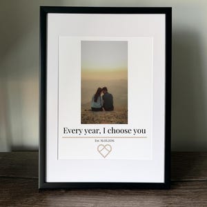Puede incluir: Impresión enmarcada en negro con paspartú blanco. La impresión muestra una pareja al atardecer, con el texto "Every year, I choose you", un símbolo de corazón y la fecha "Est. 16.05.2016".