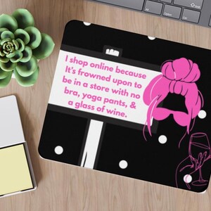 May include: Black mousepad with a pink illustration of a woman with a bun and a glass of wine. The mousepad has the text: "I shop online because It's frowned upon to be in a store with no bra, yoga pants, & a glass of wine."