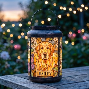 May include: A cylindrical lantern with a dark brown metal frame and handle, featuring a stained glass panel depicting a golden retriever dog surrounded by white flowers and a purple butterfly, with the name BAILEY printed on a rectangular plaque.