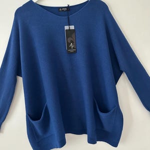 May include: A blue knitted jumper with long sleeves and two large pockets. The jumper has a round neckline and is made of a soft, comfortable fabric. The tag on the jumper reads "A.F. ALDO KNITWEAR".