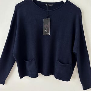 May include: A navy blue sweater with a crew neck and two front pockets. The sweater has long sleeves and a tag with the brand name. The sweater is hanging on a white hanger.