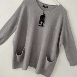 May include: A grey oversized sweater with two large pockets on the front. The sweater has a round neckline and long sleeves. The sweater has a tag that says "4F" on it.