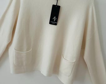 May include: Cream-coloured sweater with a crew neck and two front pockets. The long-sleeved knitwear has a relaxed fit and a tag with the brand name "ALPIN KNITWEAR". The sweater is hanging on a white hanger.