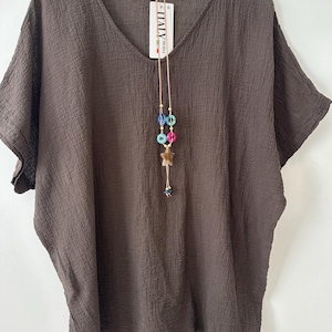 May include: A brown, textured V-neck top with short sleeves hanging on a white hanger. A long necklace with colourful beads and a star pendant hangs from the neckline. A tag that says "ITALY MODA" is attached to the top.