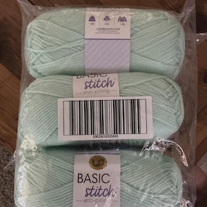 May include: Three packaged skeins of mint green yarn. Each skein is labelled with "BASIC stitch anti-pilling" and a barcode. The packaging is clear plastic, and the yarn is tightly wound.