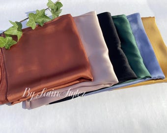 May include: A stack of seven different colored satin scarves. The scarves are arranged in a fan shape, with the top scarf being a burnt orange color. The other scarves are beige, black, dark green, light blue, and gold.