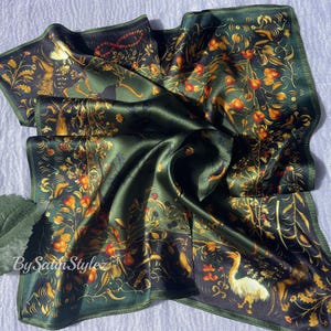 May include: A green silk scarf with a floral and animal print. The print features a variety of birds, flowers, and other botanical elements. The scarf is folded and displayed on a white surface.