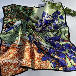 May include: Silk scarf with a colorful floral design featuring irises in shades of blue and green, with orange and yellow accents. The scarf has a black border and the text "By Laim Style".