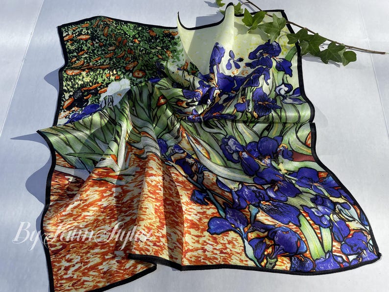 May include: Silk scarf with a colorful floral design featuring irises in shades of blue and green, with orange and yellow accents. The scarf has a black border and the text "By Laim Style".