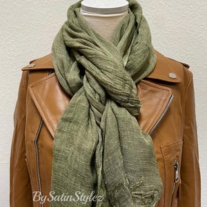 May include: A green linen scarf with a frayed edge is draped around a brown leather jacket. The scarf is tied in a loose knot at the neck. The text "By Satin Stylez" is visible on the scarf.