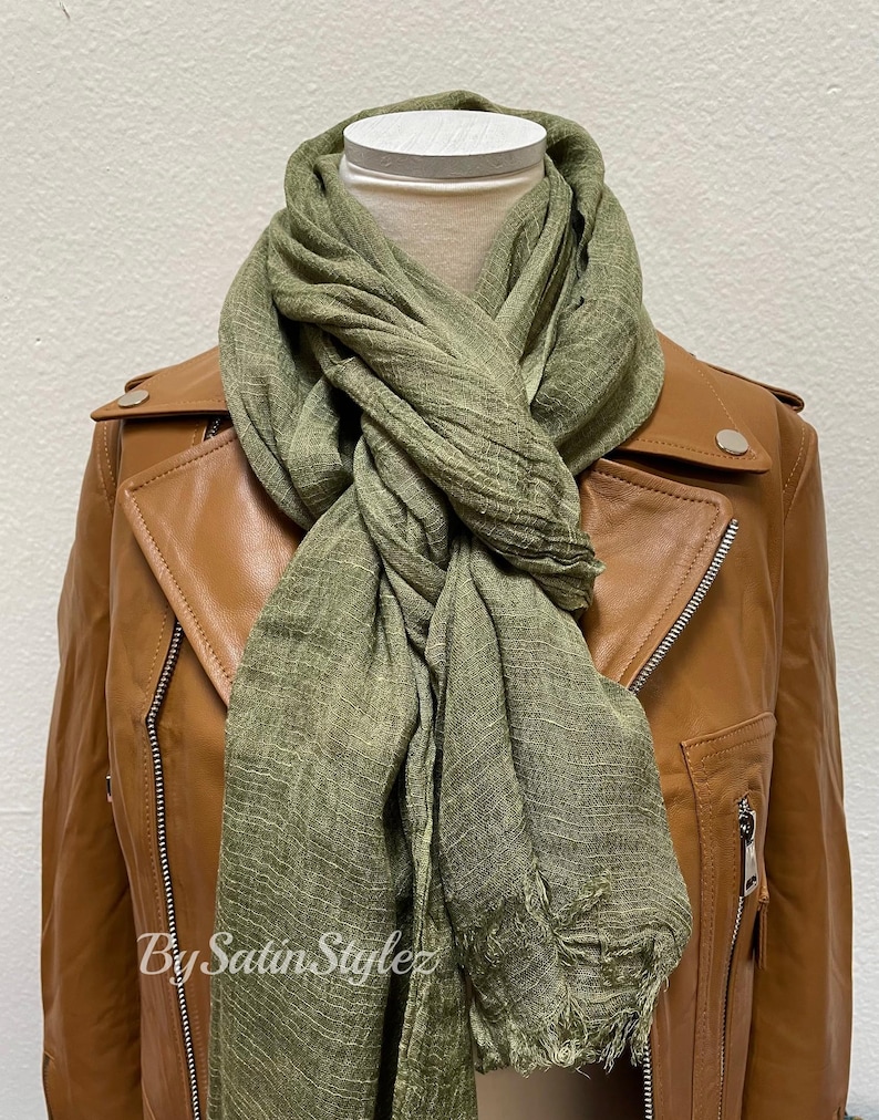 May include: A green linen scarf with a frayed edge is draped around a brown leather jacket. The scarf is tied in a loose knot at the neck. The text "By Satin Stylez" is visible on the scarf.