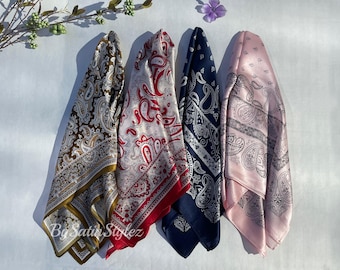 May include: Four paisley patterned silk scarves in different colors: brown, red, blue, and pink. The scarves are arranged in a row, with the brown scarf on the left and the pink scarf on the right.
