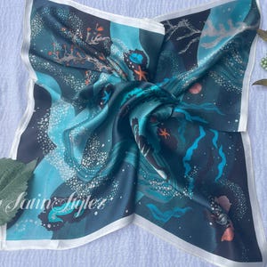 May include: Square silk scarf with an ocean-themed design. The scarf features a dark teal background with illustrations of coral, starfish, and other marine life in shades of teal, blue, and orange. The scarf has a white border and the text "By Satin Stylez".